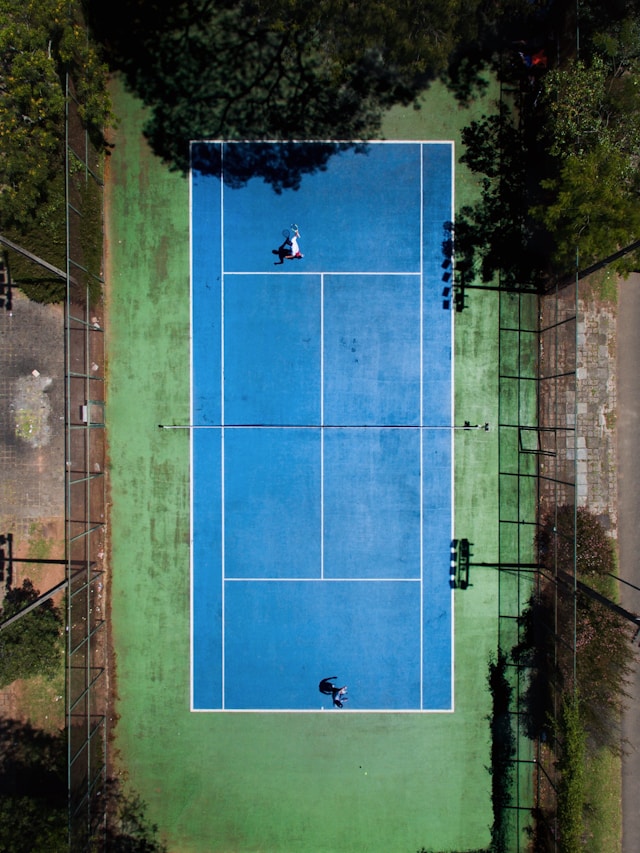 Beginner tennis player receiving instruction from coach on outdoor court, showing the welcoming nature of tennis for newcomers